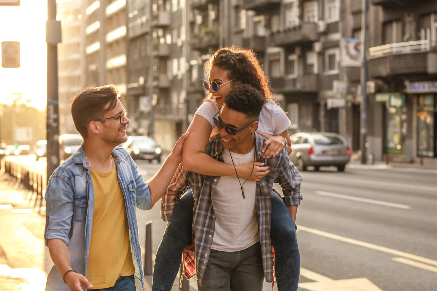 three friends walking down a city sidewalk, one is carrying another on their back
