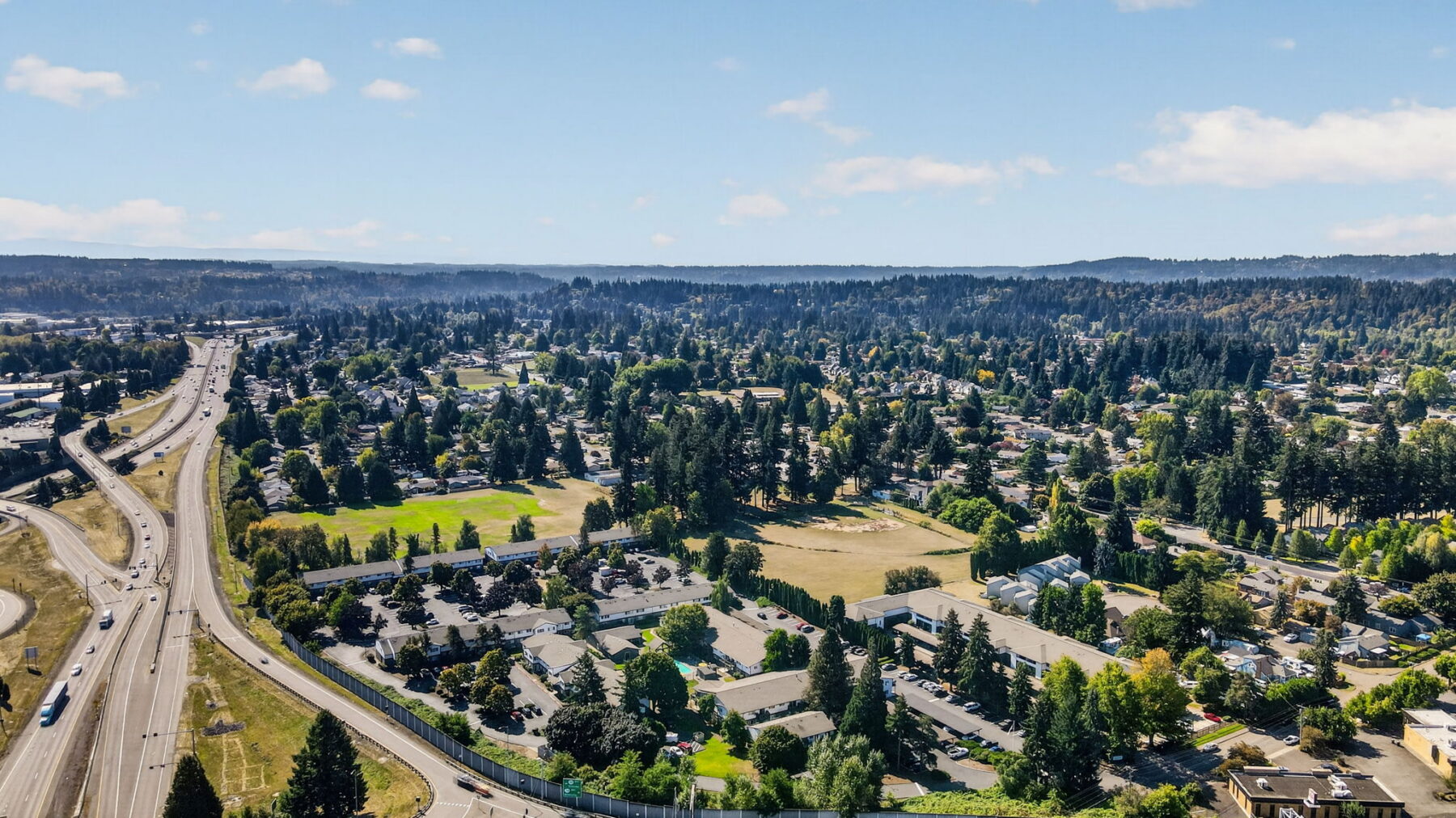 Aerial view of a suburban neighborhood with highways, houses, trees, and green spaces under a sunny, blue sky near Downtown Denver.